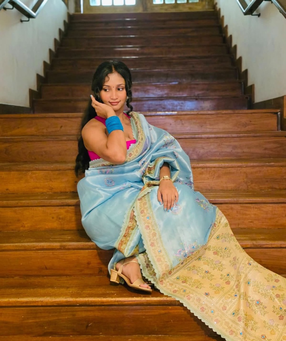 Thaara seated on a wooden staircase in a blue saree